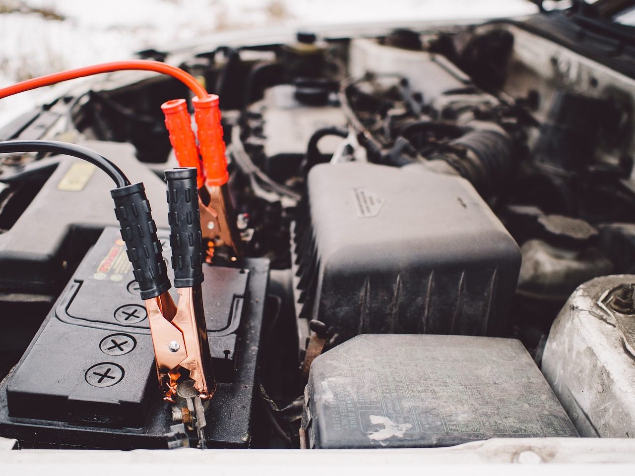 Jumper cables clamped to a car battery under an open hood