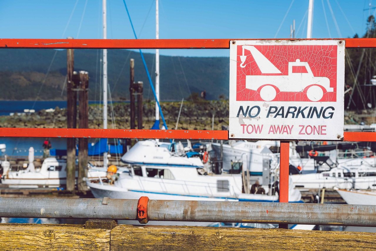 A tow-away No Parking sign on a railing, with moored boats behind it