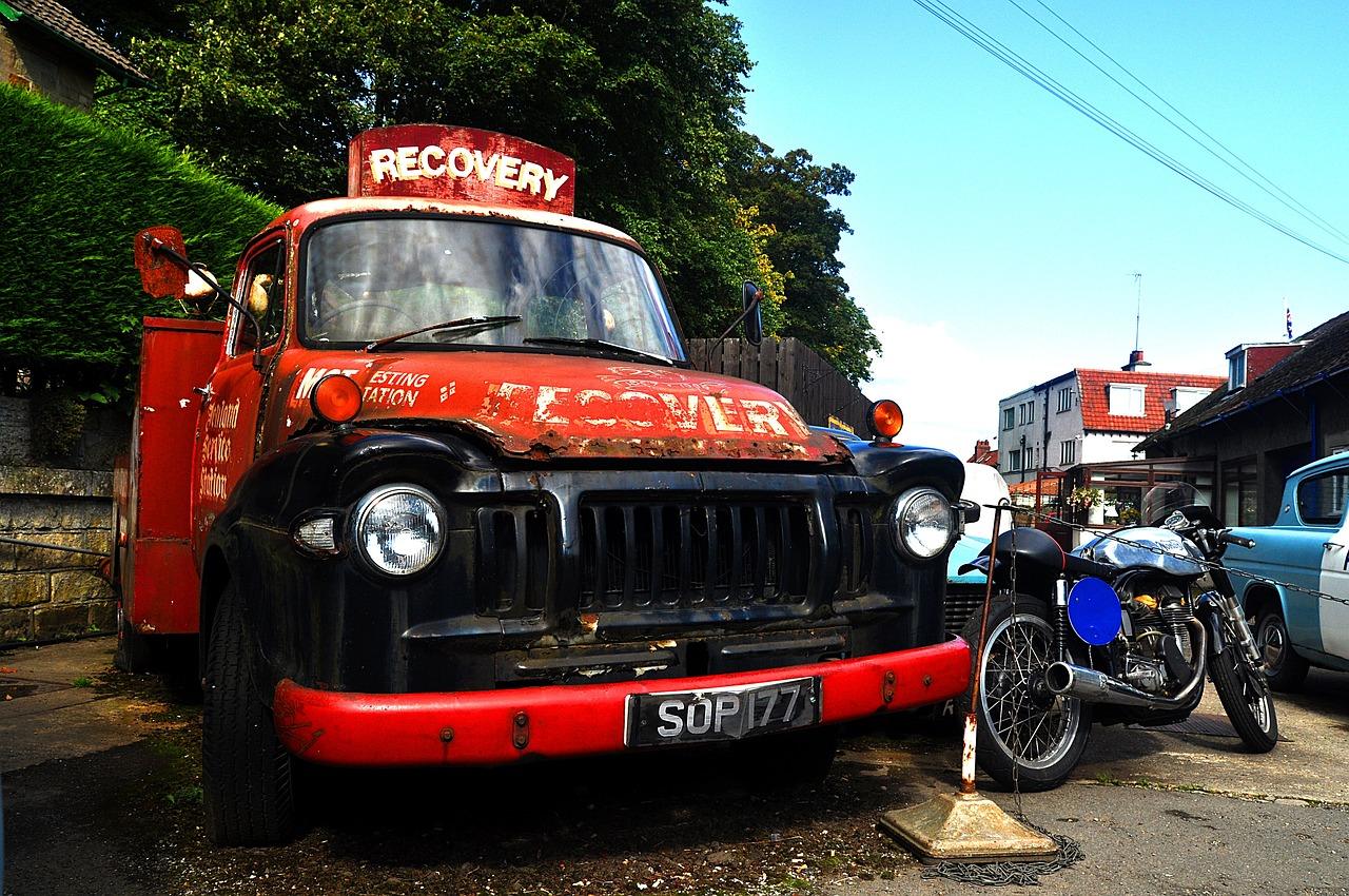 A vintage recovery tow truck parked beside a motorcycle, with no one in view
